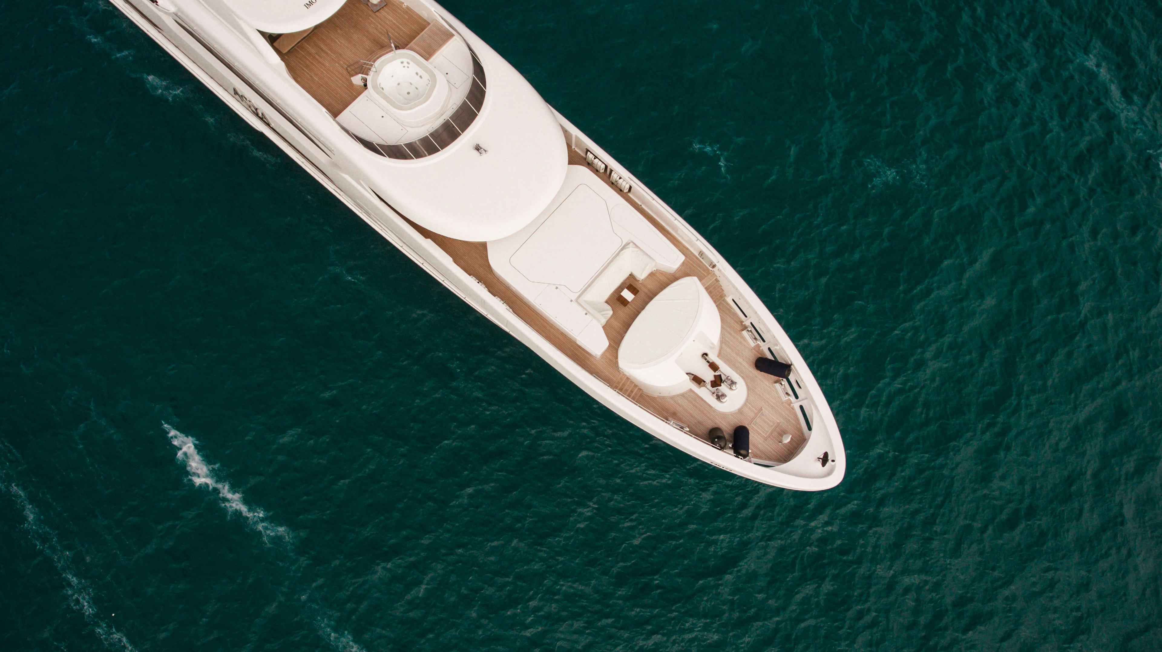 Aerial detail of a yacht’s bow and teak foredeck above turquoise water